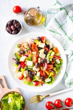 Greek salad on white. Vegetable salad with tomato, cucumber, feta cheese and olive oil. Top view on white stone table.