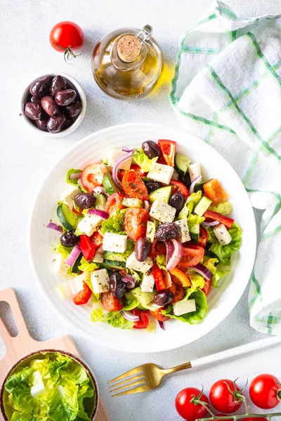Greek salad on white. Vegetable salad with tomato, cucumber, feta cheese and olive oil. Top view on white stone table.