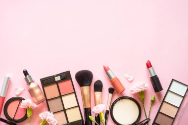 Makeup professional cosmetic products on pink with flowers. Flat lay image with copy space.