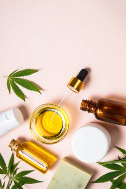Esrar esaslı yağ, krema, sabun ve pembe arka planda taze yeşil yapraklar. Doğal kozmetik. Kopyalama alanı olan düz.