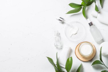 Doğal Kozmetik Laboratuarı. Kozmetik şişeleri, krem, serum, deniz tuzu ve yeşil yapraklar beyaz masada. Düz görünüm.