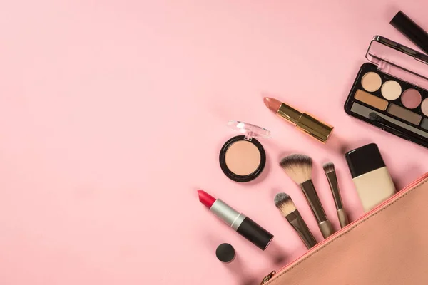 Make up products at pink background with cosmetic bag. Eye shadow, lipstick, powder, brushes and more for professional make up. Flat lay image.