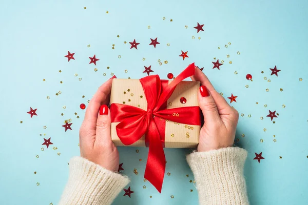 Christmas present box with red ribbon. Woman is giving a present. Flat lay image on blue.