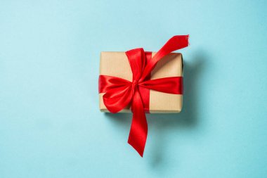 Kırmızı kurdeleli ve parıltılı Noel hediyesi kutusu. Mavi üzerine düz resim yatıyordu.