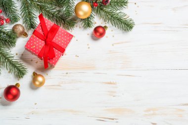Kırmızı kurdeleli ve Noel süslemeli Noel hediyesi kutusu. Beyaz ahşap masadaki en üst manzara.