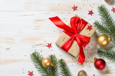 Kırmızı kurdeleli ve Noel süslemeli Noel hediyesi kutusu. Tebrik kartı. Beyaz ahşap masadaki en üst manzara.