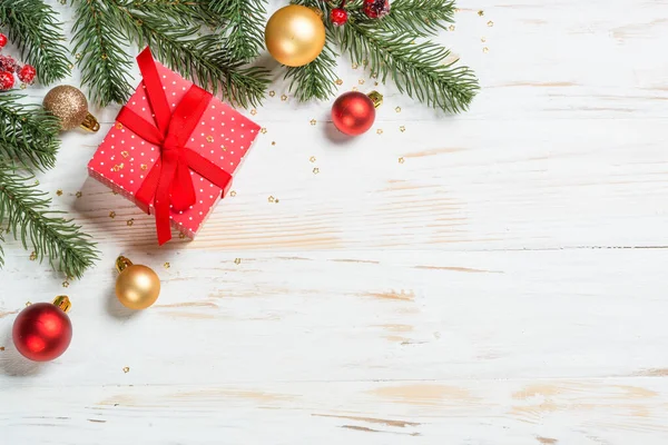 Kırmızı kurdeleli ve Noel süslemeli Noel hediyesi kutusu. Beyaz ahşap masadaki en üst manzara.