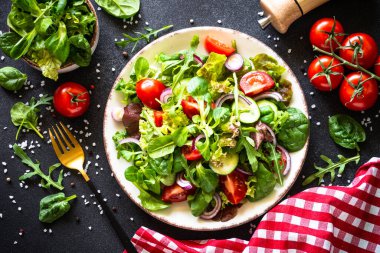 Siyah masada beyaz tabakta salata yaprakları ve sebzeler. İçerikli üst görünüm.