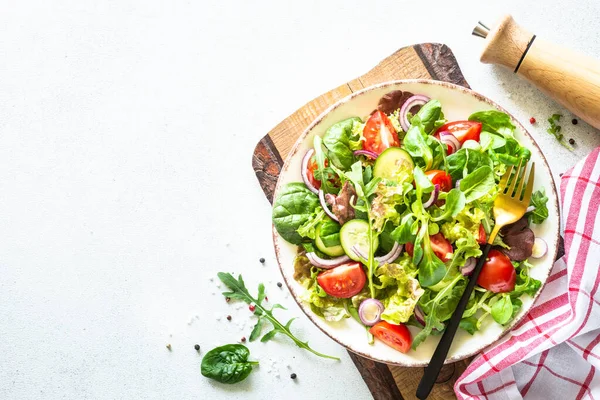 Green salad, veggie dish. Fresh salad leaves and vegetables in white plate. Healthy vegan food, diet food. Top view image.