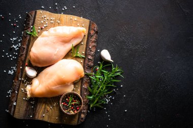 Baharatlı tavuk filetosu ve siyah taş masadaki tahta kesme tahtasındaki bitkiler. Çiğ et ve malzemeler. Kopyalama alanı olan üst görünüm.
