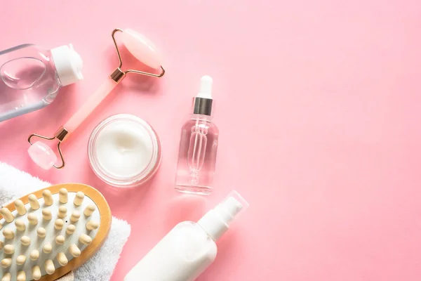 Natural cosmetics on pink. Skin care product, cream, soap serum, jade roller and white towel. Flat lay image with copy space.