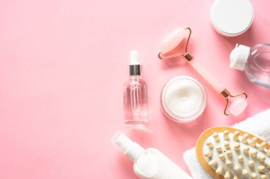Natural cosmetics on pink. Skin care product, cream, soap serum, jade roller and white towel. Flat lay image with copy space.