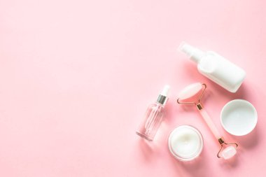 Deri bakımı konsepti. Yeşim bigudi, krema ve serum şişesi pembeye. Kopyalama alanı olan düz resim.