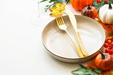 Süslemelerle birlikte beyazı sonbahar masasına koyun. El işi tabağı, altın çatal bıçak, cam, mum ve sonbahar süslemeleri..