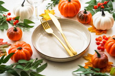 Sonbahar sofrası. Tatil yemeği. El işi tabağı, altın çatal bıçak, cam, mum ve sonbahar süslemeleri..