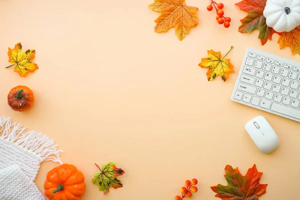 Autumn office workspace. Autumn flat lay background. Keyboard, laptop with autumn cloth and fall decorations - pumpkin, leaves and other.