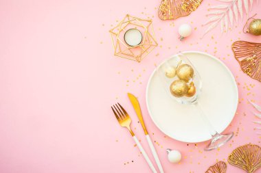 Beyaz tabak ve pembe arka planda noel süslemeleri olan bir Noel masası. Düz görünüm.