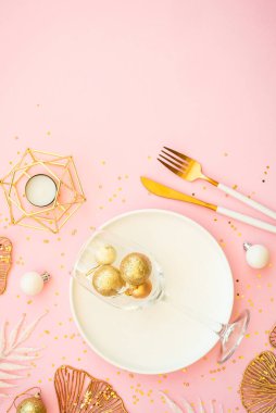 Beyaz tabak ve pembe arka planda noel süslemeleri olan bir Noel masası. Düz görünüm.