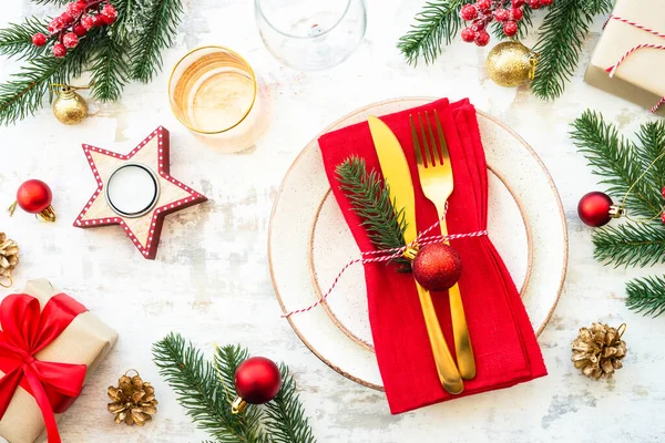 Christmas food, christmas table setting with white plate, golden cutlery and christmas decorations on white wooden background. Top view.