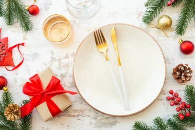 Beyaz tabak, altın çatal bıçak takımı, hediye kutusu ve beyaz ahşap arka planda noel süslemeleri. Üst görünüm.