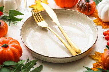 Sonbahar sofrası. Tatil yemeği. El işi tabağı, altın çatal bıçak, cam, mum ve sonbahar süslemeleri..