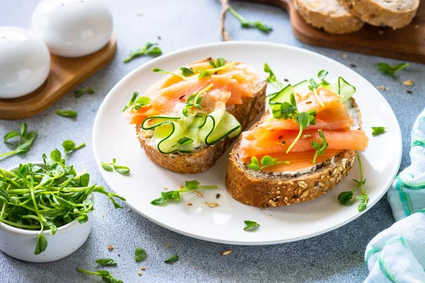 Krem peynirli, somonlu ve beyaz tabakta salatalıklı sandviç. Sağlıklı kahvaltı ya da atıştırmalık. Kapat..