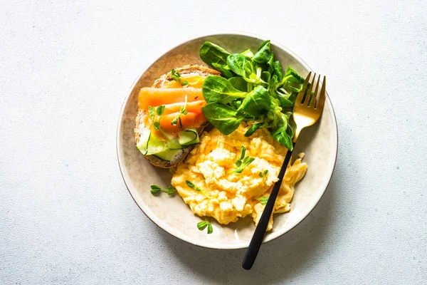 Çırpılmış yumurta, krem peynirli sandviç, somon balığı ve beyaz taş masada salata yaprakları. Üst görünüm.