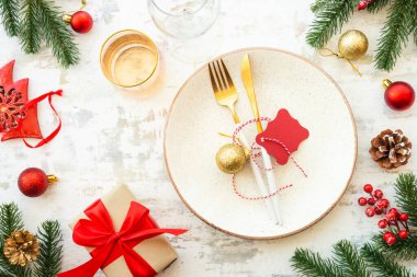 Noel yemeği, beyaz tabaklı Noel masası takımı, altın çatal bıçak takımı ve beyaz ahşap arka planda noel süslemeleri. Üst görünüm.