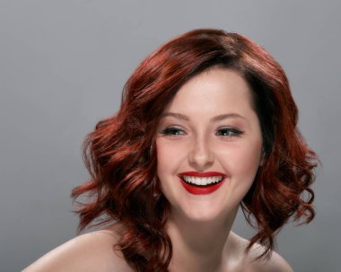 Gülümseyen kızıl saçlı, kıvırcık saçlı bir kadının portresi.