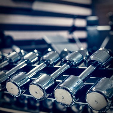 Rows of metal dumbbells for training on rack in modern gym, image with vintage toning