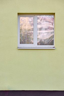 Window with white frame on the background of yellow stone wall