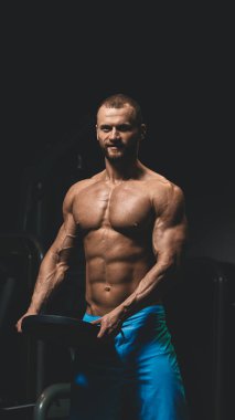 Halterle egzersiz yapmaya hazırlanan yakışıklı vücut geliştiricinin tam fotoğrafı.