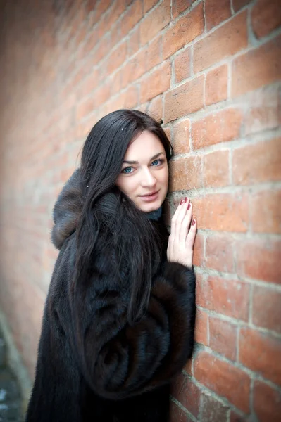 Menina bonita no inverno contra uma parede de tijolo — Fotografia de Stock