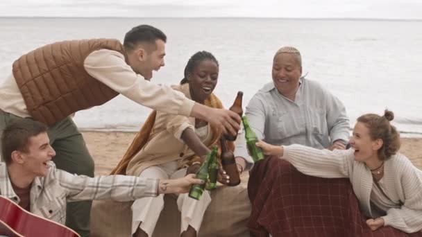 中长的五个快乐的多民族朋友坐在沙滩上 喝啤酒 在阴天聊天 — 图库视频影像