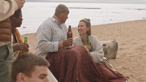 在阴天里 一群混血儿和白人妇女坐在沙滩上 与种植庄稼的朋友坐在一起 喝啤酒 — 图库视频影像