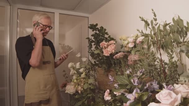 花との問題について電話で議論するストレスのあるシニア男性労働者や小さな花屋の所有者の中程度のショット — ストック動画