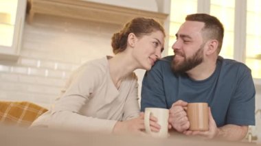 Sabahları kahve fincanlarını tutarak, gülümseyip konuşarak mutlu, genç, beyaz eşlerin orta boy fotoğrafları.