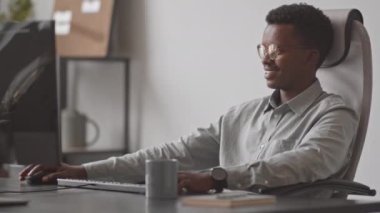 Genç Afro-Amerikan erkek programcının iş yerinde bilgisayar monitörünün önünde oturduğu belden yukarısını çekerek yeni yazılımlar geliştiriyor.