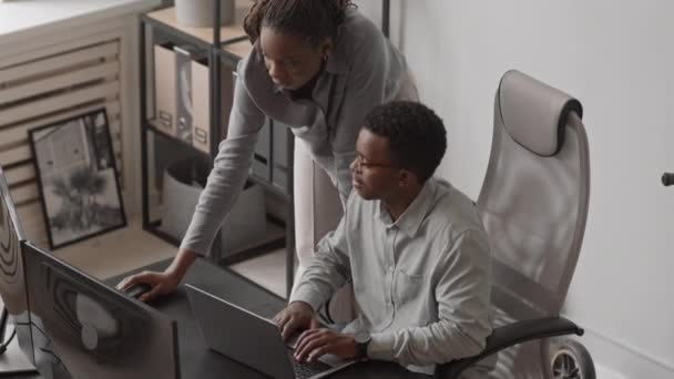 在现代办公室里 一对年轻的非裔美国人程序员一起在新软件上工作 看着电脑显示器在对话 拍下了一张高角度的照片 — 图库视频影像