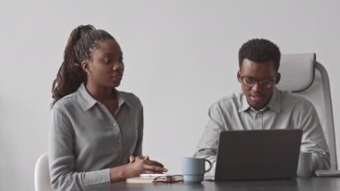 Bir çift genç Afro-Amerikalı programcının dizüstü bilgisayarda yeni yazılım geliştirmeyi tartışırken belden aşağısı, ofiste gri duvarın karşısında oturuyor.