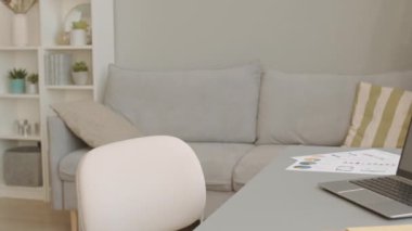 Minimalist ev ofisinde arka planda rahat bir kanepe ile pencerenin önünde iş belgeleriyle gri çalışma masasını görüntüleyen kimse yok.