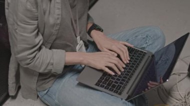 Zeminde oturan, taşınabilir bilgisayarın klavyesinde yazan yüksek açılı kadın programcı.