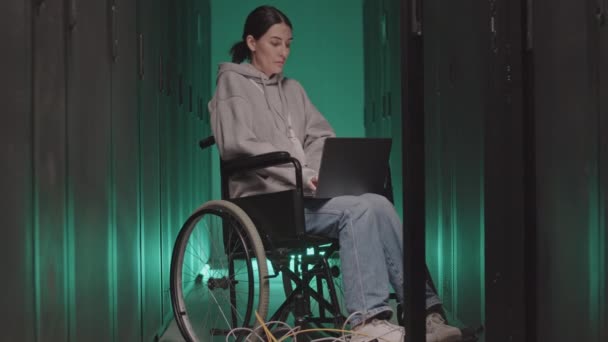 車椅子の白人女性のフルショット 緑の照明サーバールームでノートパソコンを入力します — ストック動画