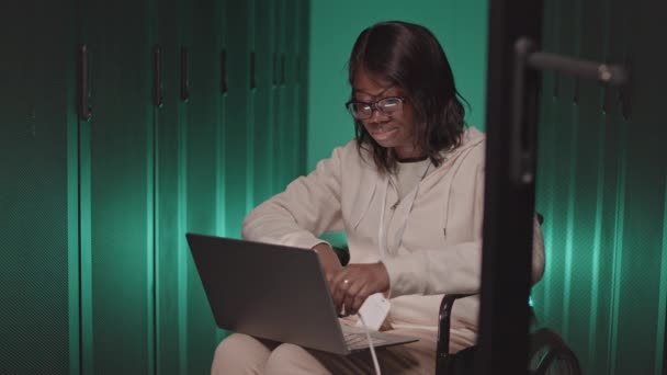 車椅子に若いアフリカ系アメリカ人女性の中長期 緑の照明データセンターでラップにポータブルコンピュータを保持 サーバーキャビネットにケーブルを差し込みます — ストック動画