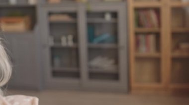 Düşünceli, yaşlı, beyaz bir kadının, gündüz vakti oturma odasında oturup, uzaklığa baktığı yakın plan çekimleri.