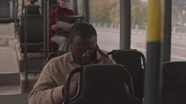 Otobüste akıllı telefondan konuşan, gülümseyen, arka planda oturan bulanık kadınların sandığı.