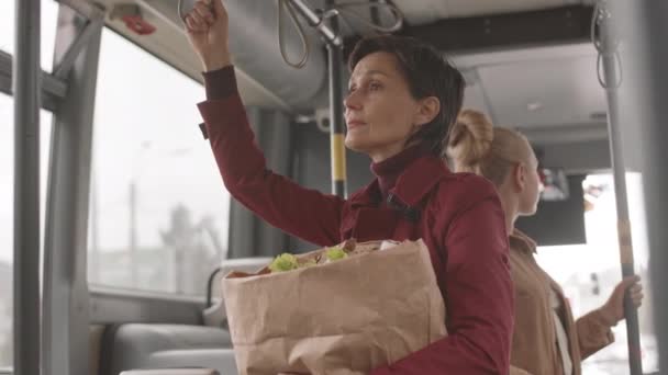 赤トレンチコートを着た短髪の白人女性の低い角度 食料品と紙袋を保持 バスに乗る — ストック動画