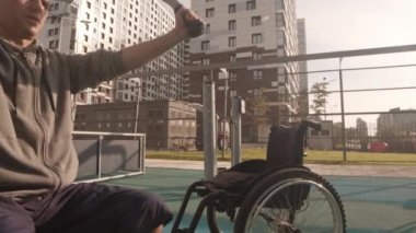 Fiziksel engelli bir beyaz adamın izini sürmek güneşli bir günde spor alanında ekipman kullanmak, tekerlekli sandalyeyle ona yaklaşmak.