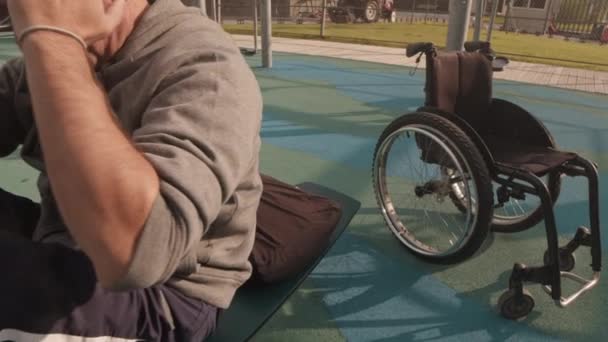夏日早晨 从轮椅追踪到白人男子在邻居家的运动场上用器械做腹肌运动 — 图库视频影像