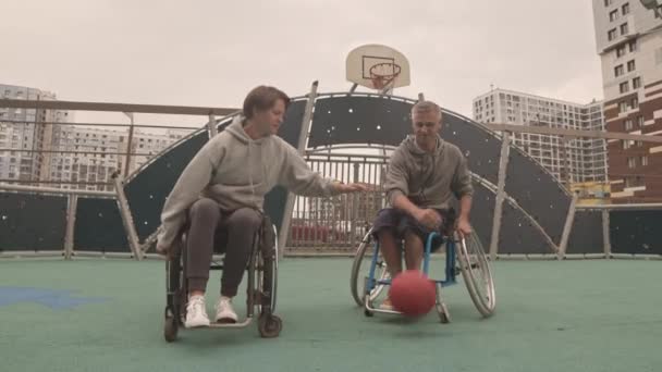 屋外裁判所でバスケットボールをしている車椅子で白人女性と男性のアマチュア選手の広いショット — ストック動画
